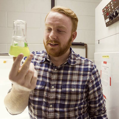 Jakob Nalley holding a flask of algae. Photo Credit: Bethany Bohlen, W.K. Kellogg Biological Station Communications and Marketing Coordinator.