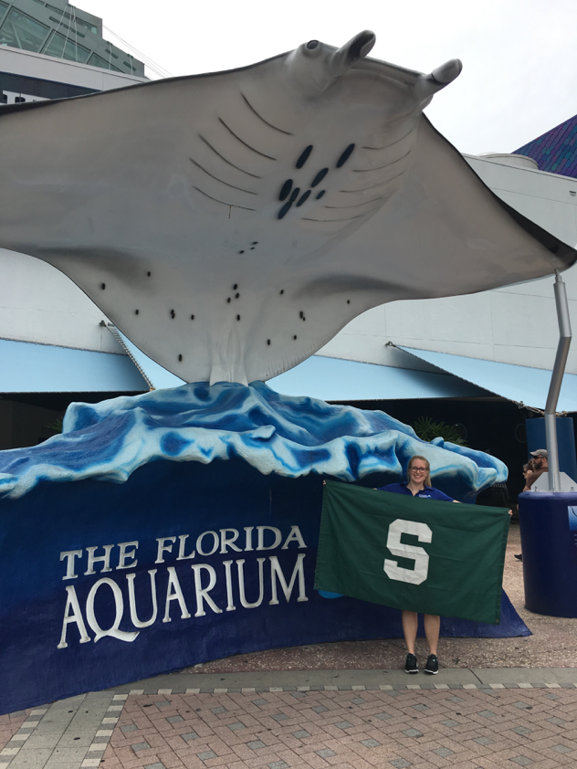 Maris Wright holding a spartan flag in front of the Florida Aquarium sign.