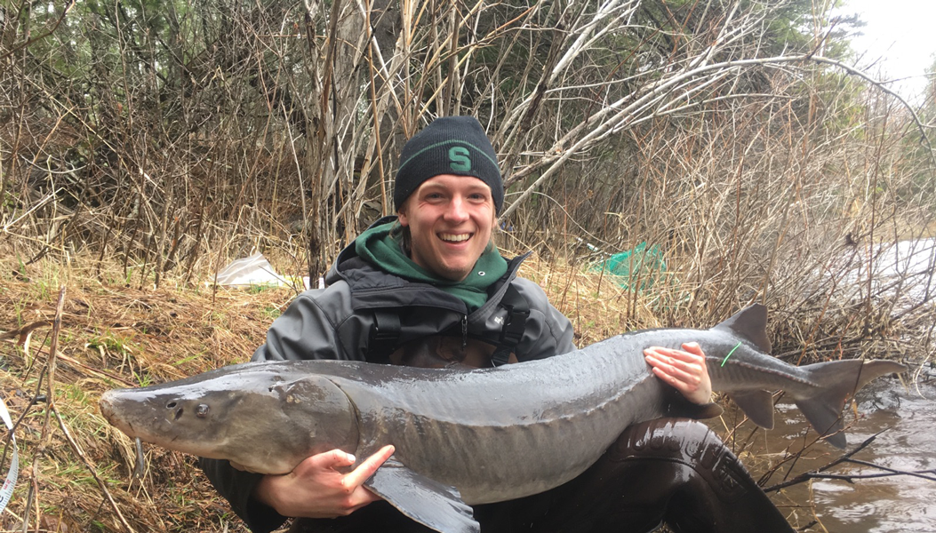 Graduate student sitting on a river bank holding a fish